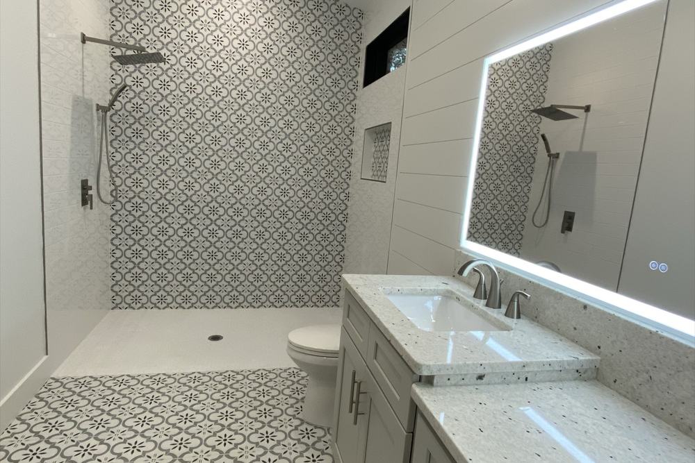 Primary bathroom with a backlit mirror, patterned tile floor and a walk-in shower