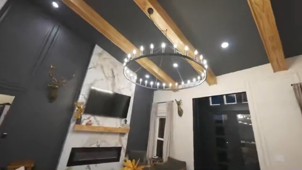 Vaulted great room with exposed beams, a ring chandelier and a linear fireplace