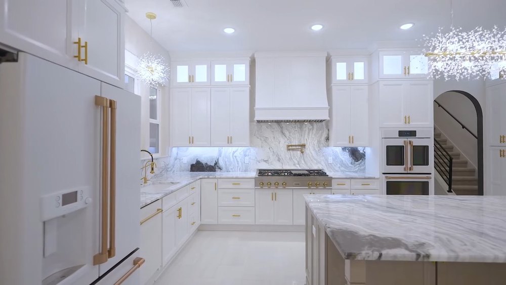 White kitchen with brass hardware, marble backsplash and a custom range hood