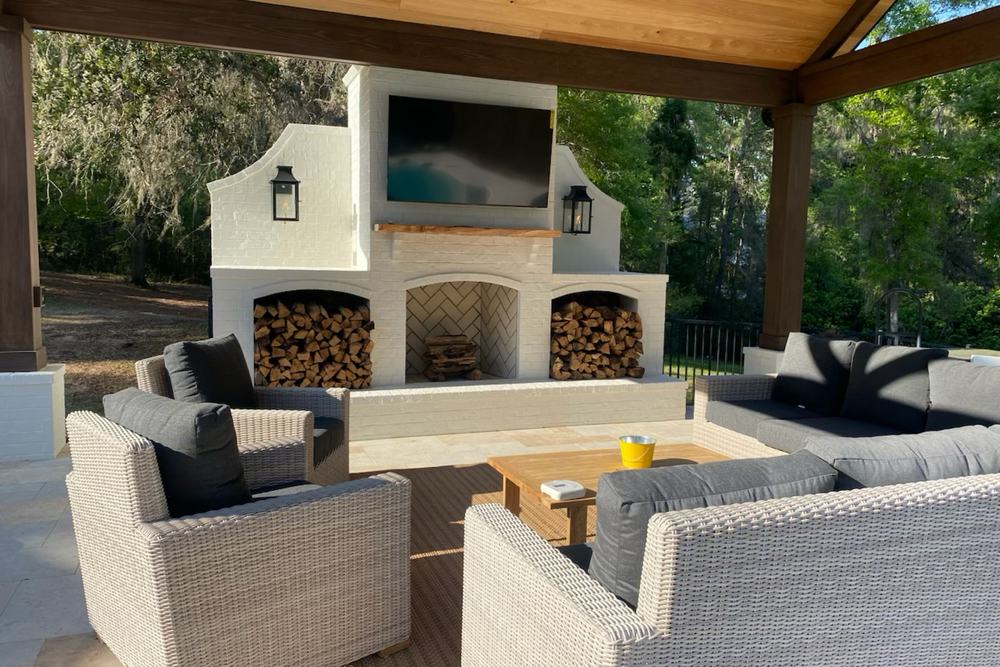 Outdoor kitchen with a masonry fireplace, mounted television and lounge seating