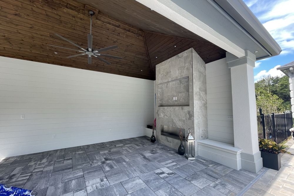 A white poolside pavilion with a stained cathedral ceiling and a marble fireplace